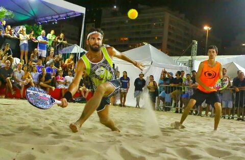 Pais assistindo seus filhos jogarem beach tennis em uma quadra de areia.