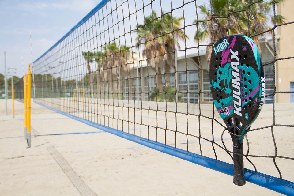 Jogador de beach tennis executando o forehand anômalo em uma quadra de areia.