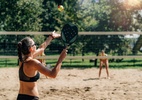 Jogador de beach tennis realizando um saque na subida em uma quadra de areia.