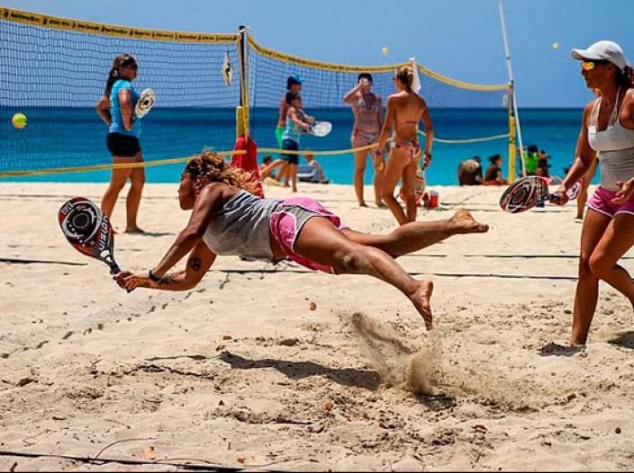 Jogador de beach tennis realizando um saque estratégico em quadra de areia.