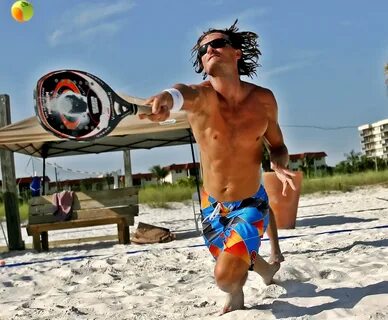 Jogador de beach tennis atacando a bola em direção ao corpo do adversário durante uma partida.