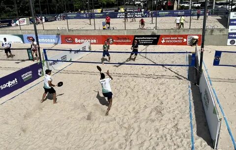 Jogador de beach tennis praticando saque em uma quadra de areia.