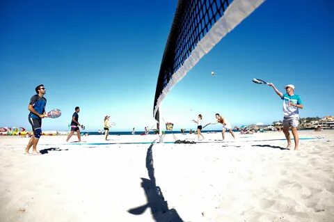 Jogador de beach tennis executando um movimento vertical em quadra de areia.