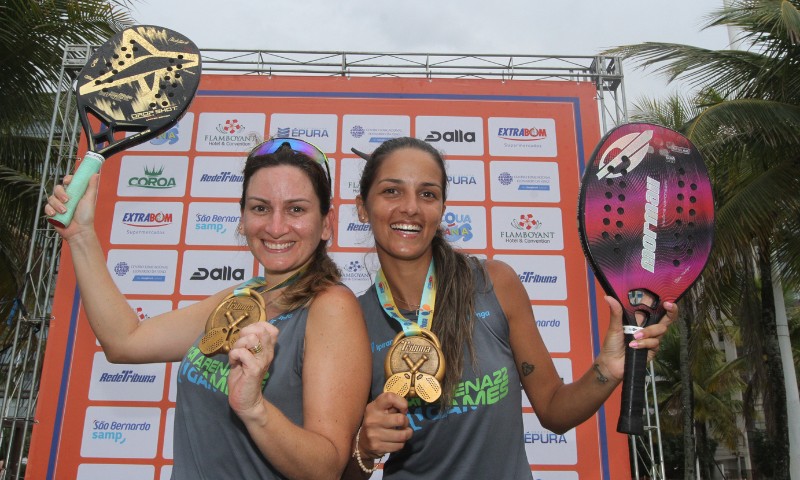 Atletas competindo no Tribuna Open de Beach Tennis na Praia de Camburi, com quadras de areia e público animado.