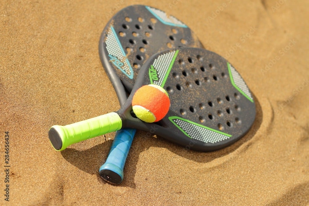 Jogadores de beach tennis em ação, destacando a prática esportiva e a importância da saúde e prevenção de lesões.