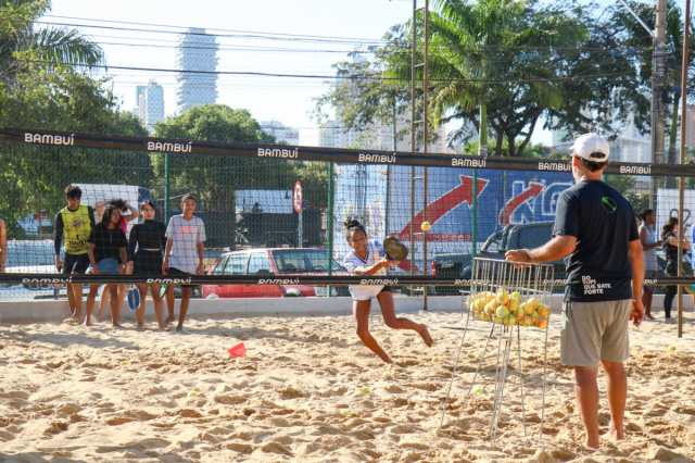 Estudantes jogando beach tennis em uma quadra de areia durante atividade escolar.