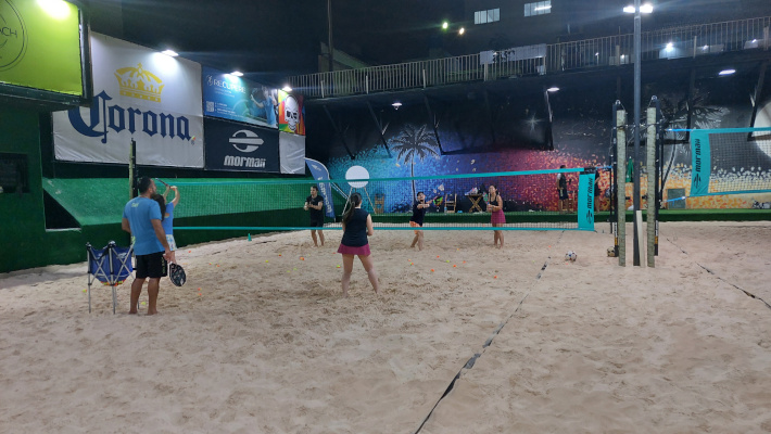 Pessoas jogando beach tennis e vôlei de praia em uma clínica ao ar livre.