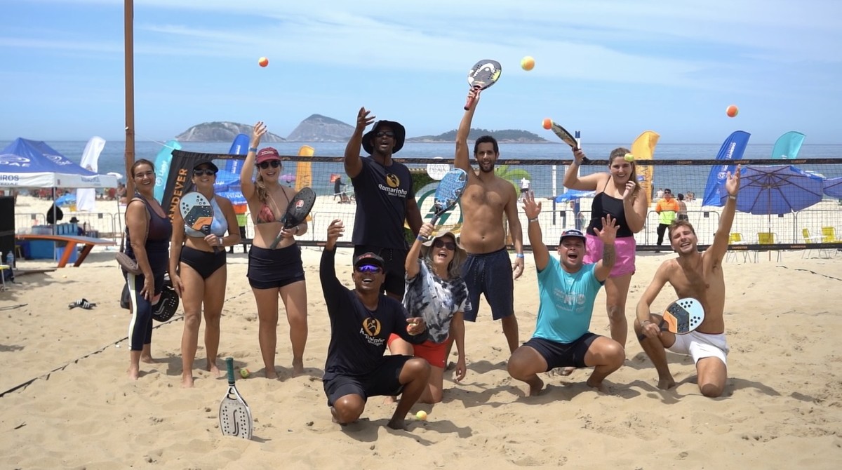 Aula de beach tennis na Praia de Ipanema, com participantes jogando sob o sol.