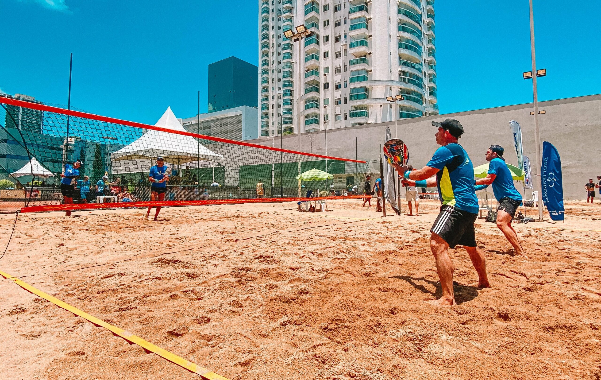 Praia de Camburi em Vitória, cenário do Campeonato Brasileiro de Beach Tennis com atletas em ação.