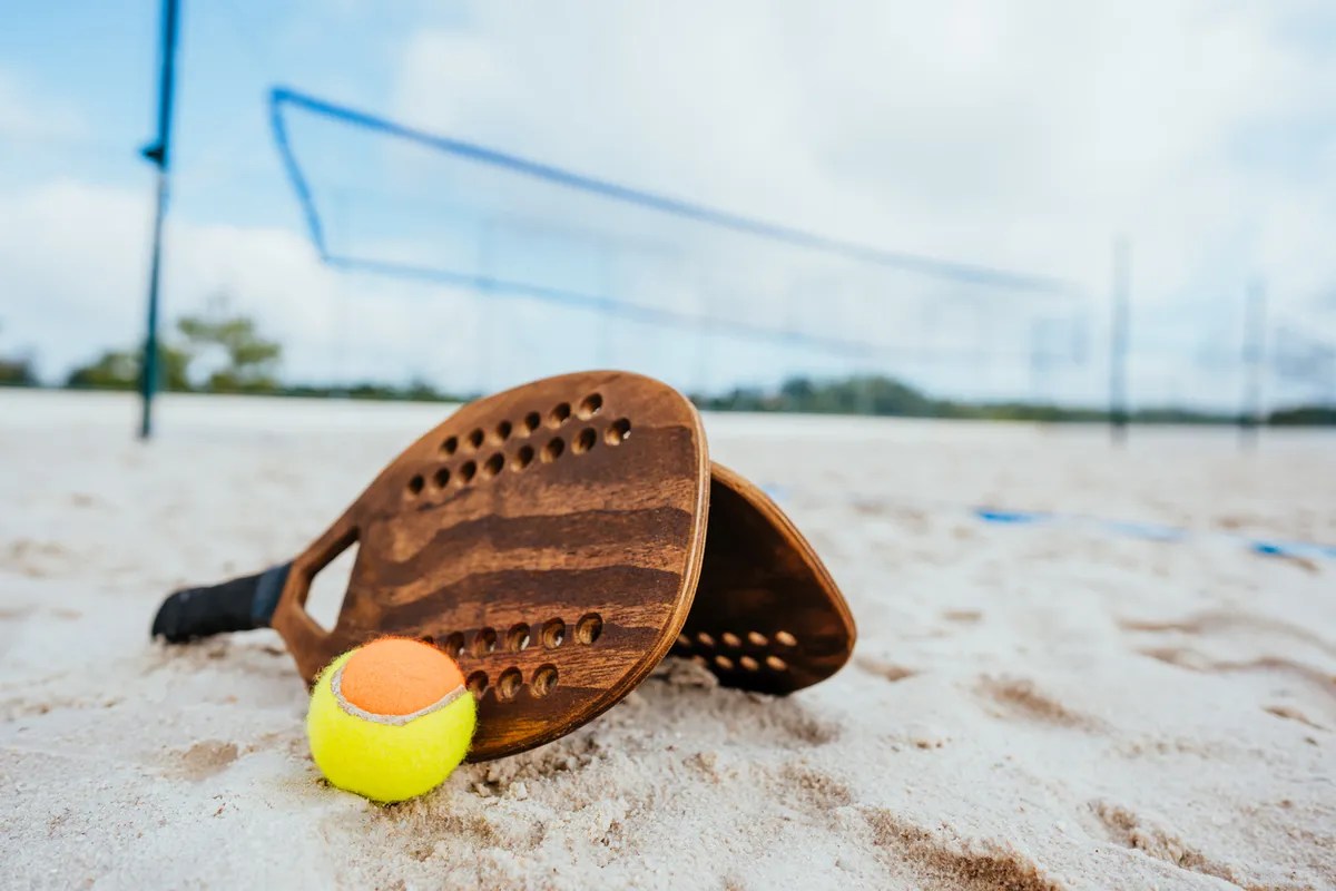 Jogadores de beach tennis se divertindo em uma quadra de areia, destacando a socialização e atividade física.