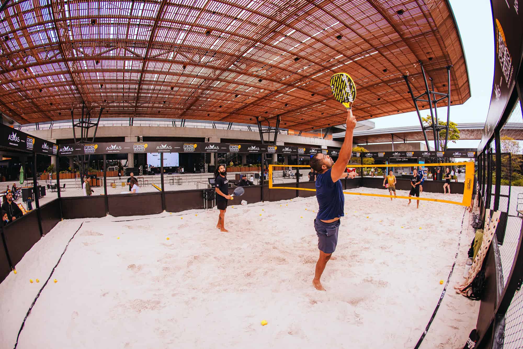 Aulões de beach tennis no Floripa Airport com participantes jogando na quadra coberta.