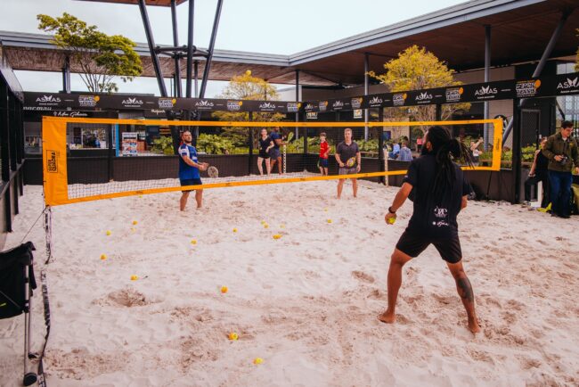 Aulões de Beach Tennis no Floripa Airport com participantes jogando na quadra de areia.