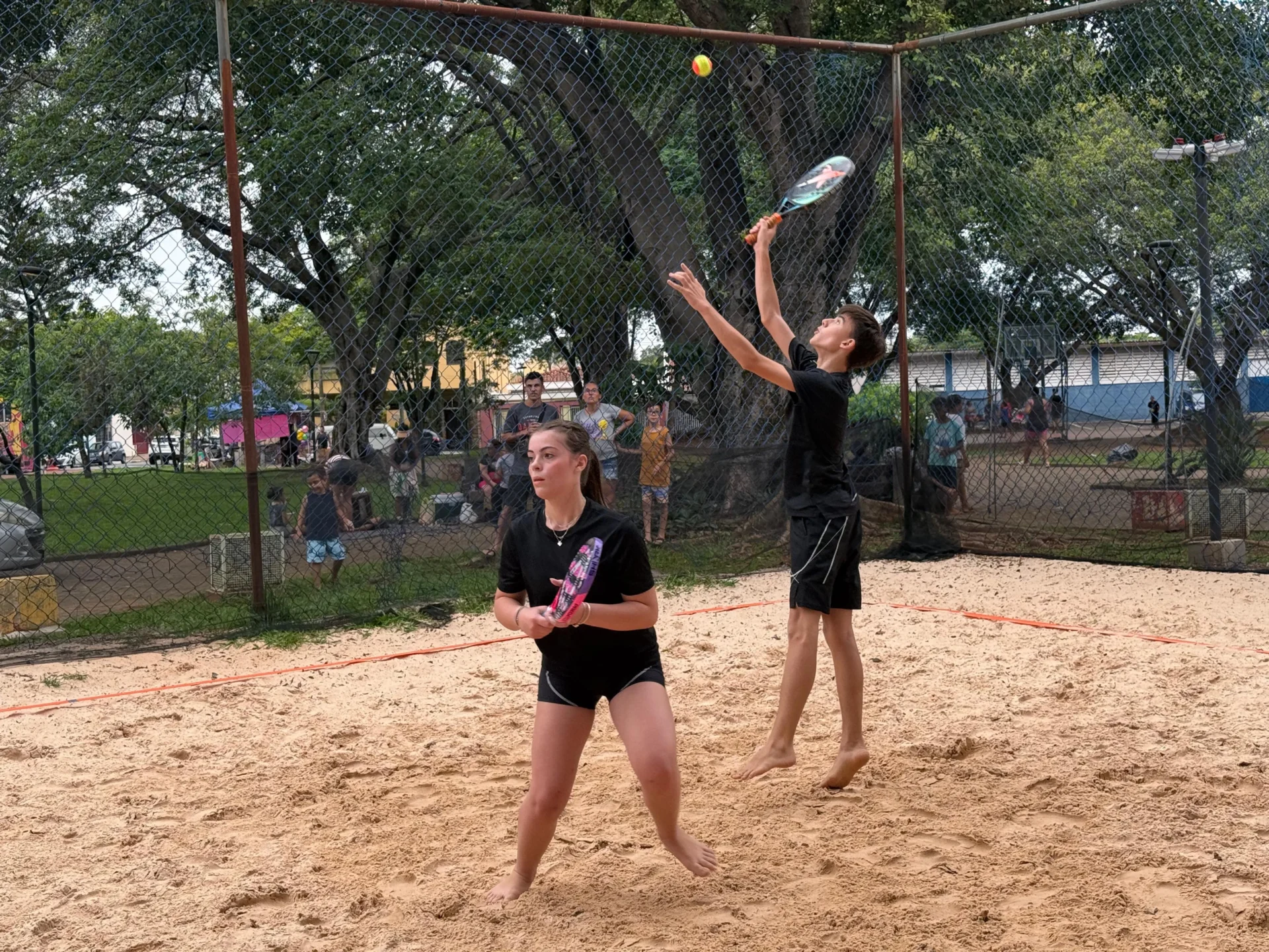 Atletas competindo no Campeonato de Beach Tennis em Cosmópolis, com quadras de areia e público animado.