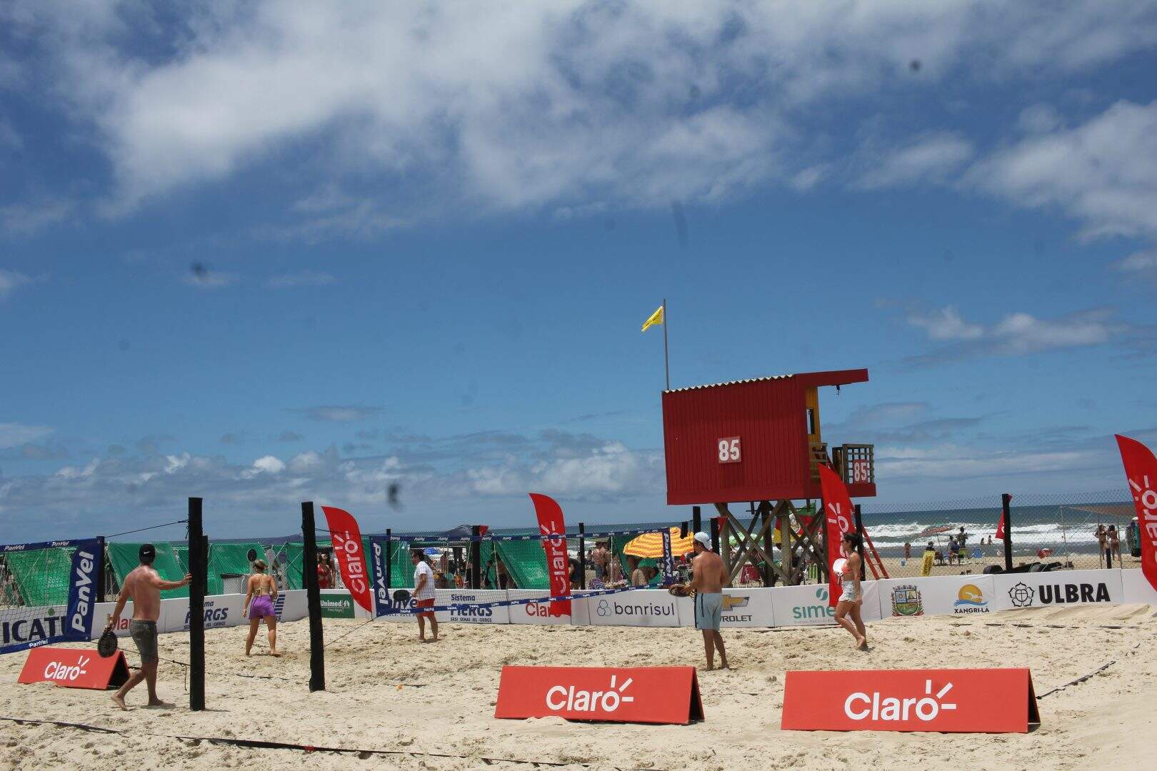 Quadras de beach tennis na Arena Rede Pampa, à beira-mar de Atlântida, com jogadores em ação.