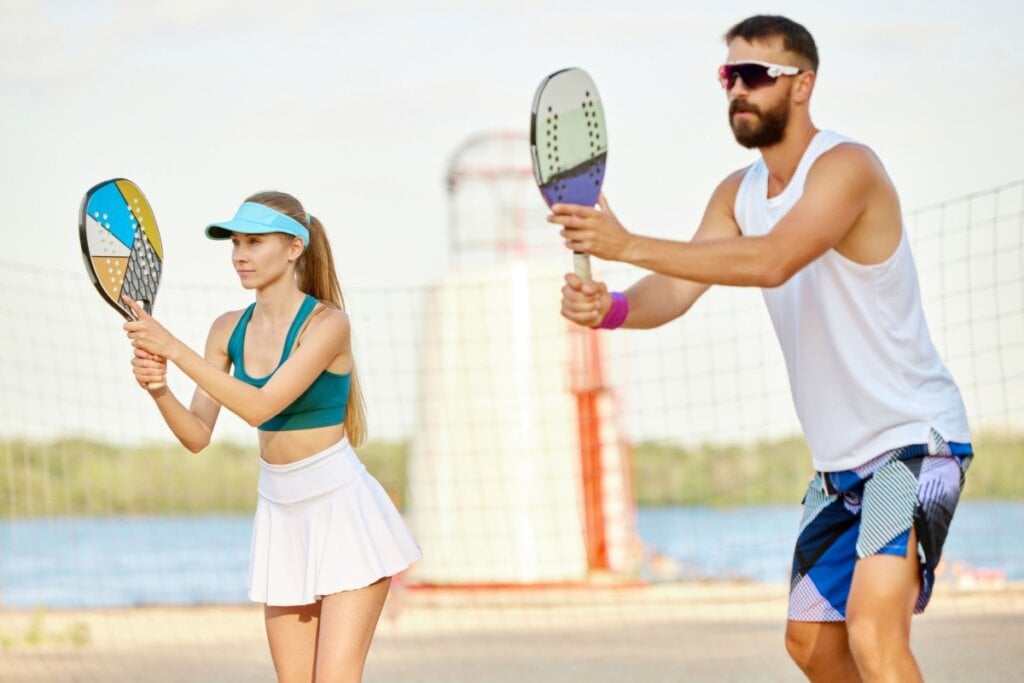 Jogadores de beach tennis em ação na areia, destacando a importância do aquecimento e técnica.