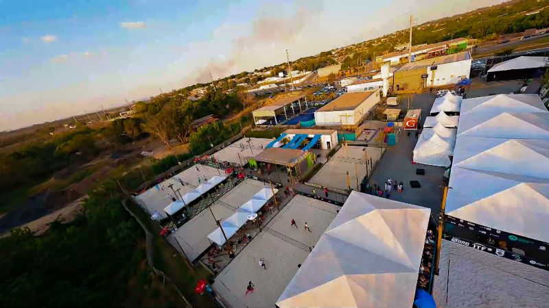 Atletas competindo em um torneio de beach tennis em Cuiabá, com quadras de areia e público animado.