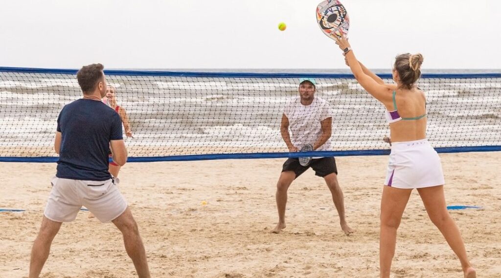 Atletas competindo em um torneio de beach tennis em Bellatorres, com público animado ao fundo.