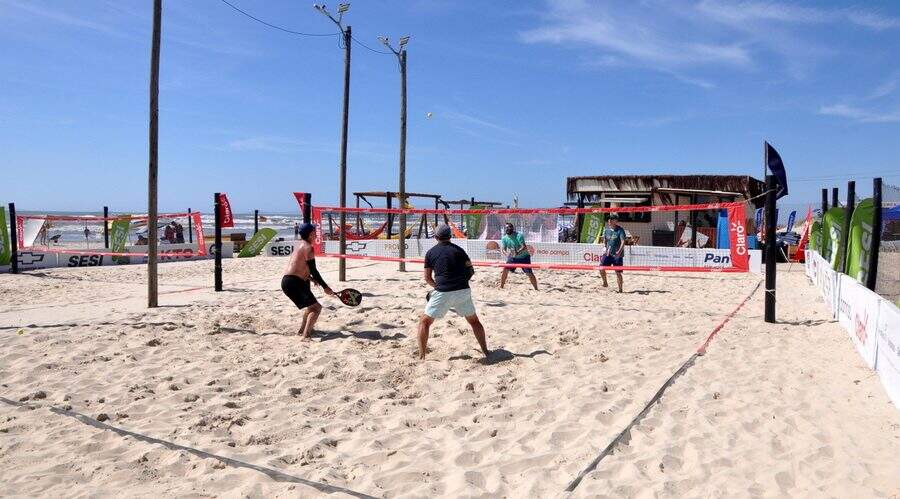 Jogadores de beach tennis se divertindo em uma quadra de areia durante uma partida.