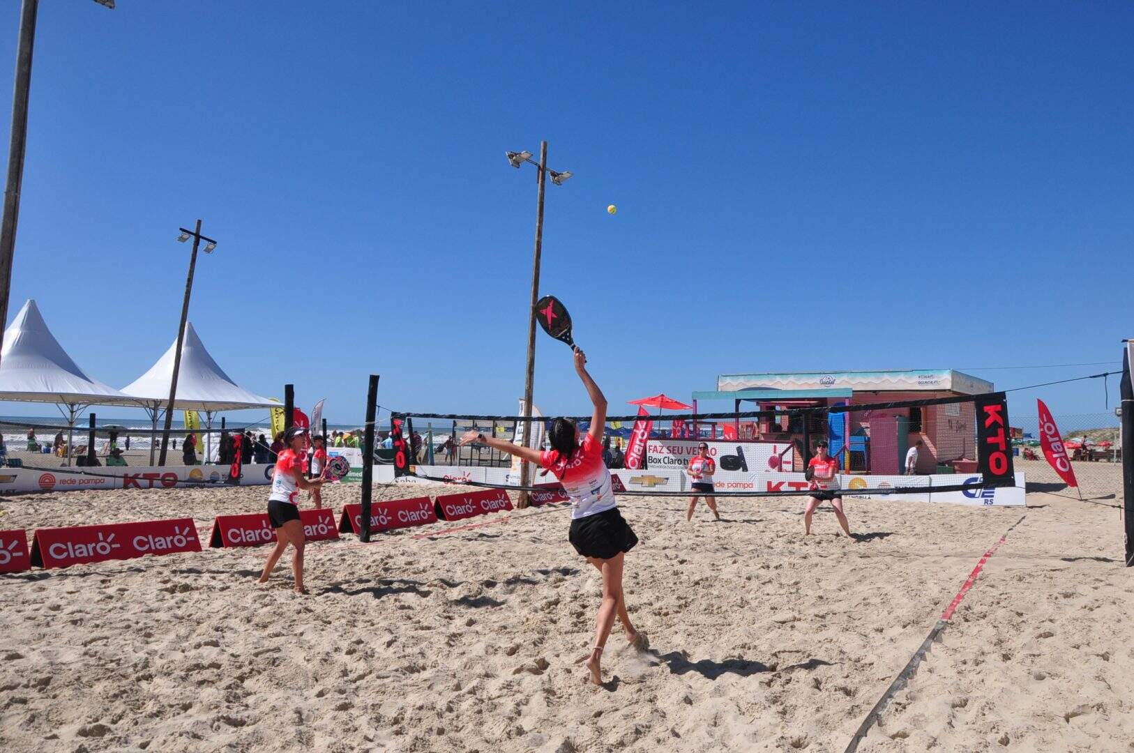 Grupo de pessoas jogando beach tennis na praia, promovendo saúde e socialização.